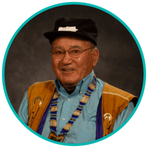 Don Honea Sr wearing his traditional Chiefs vest with Necklase, Blue button shirt in front of a Grey background.