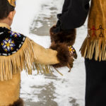 parent leading a child dressed in traditional native vest